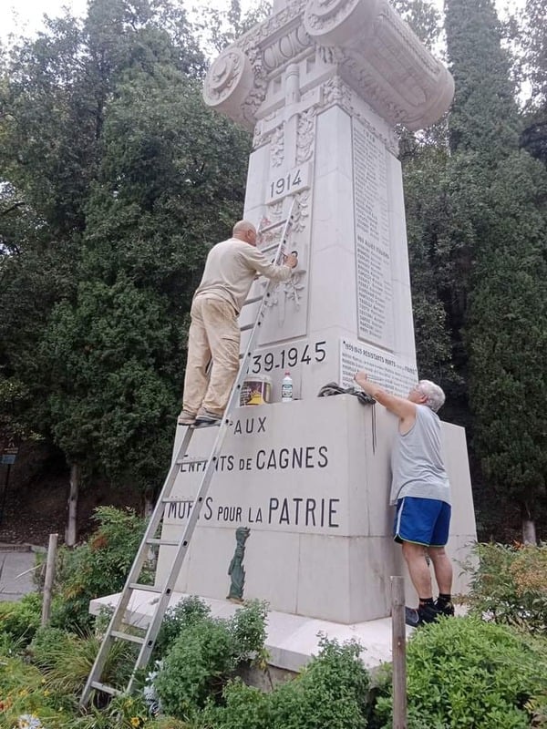 Deux compagnons sur une échelle repeignant les inscriptions d'un monument aux morts de Cagnes